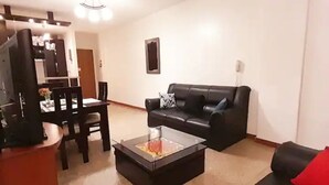 Een woonkamer met een zwarte leren bank, een glazen salontafel en een eetgedeelte met een houten tafel en stoelen.