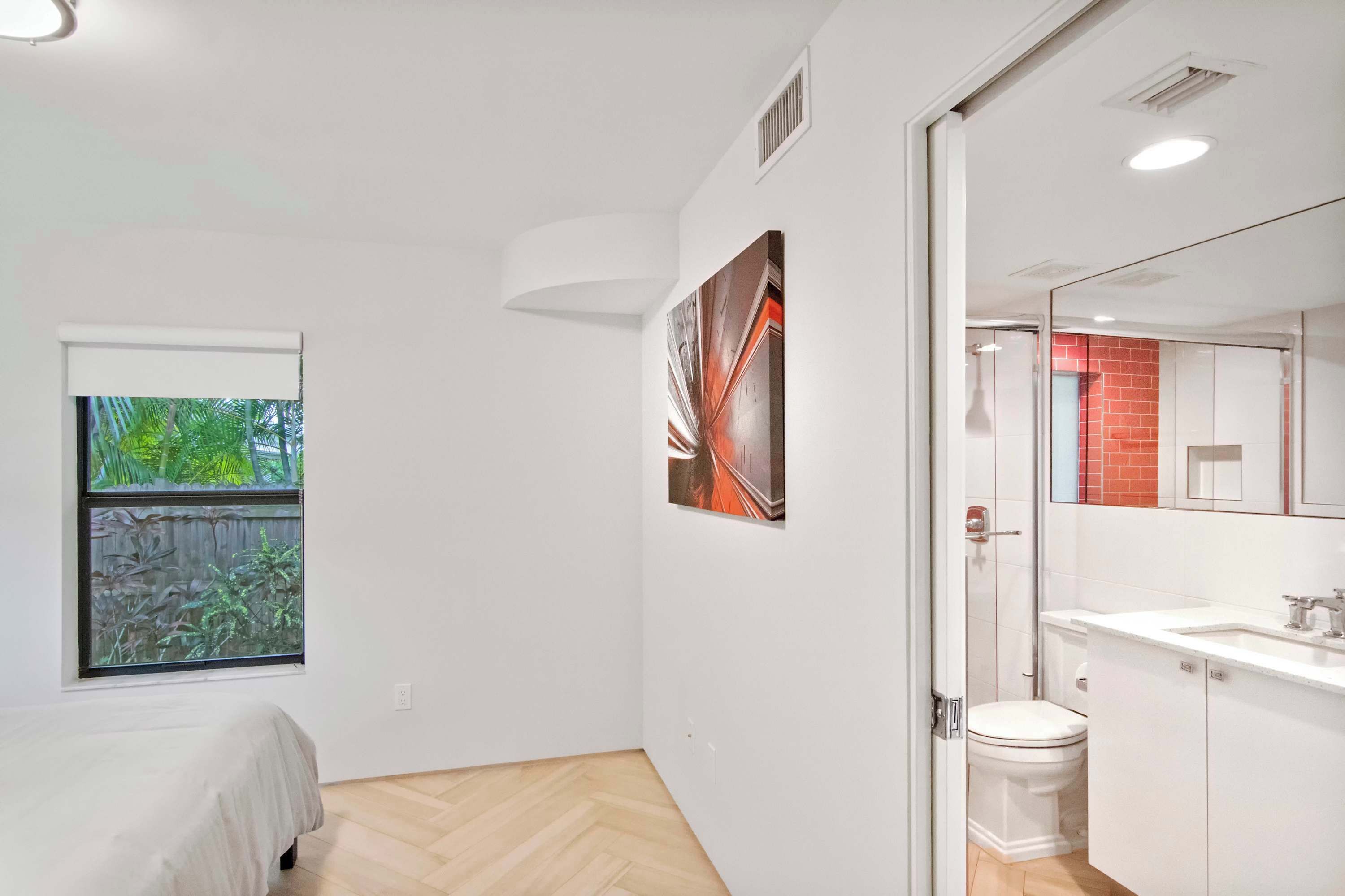 A modern bathroom with a white toilet, a sink, and a mirror. There is a window with a view of greenery outside.