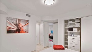 A modern bedroom with a large bed, a walk-in closet, and a hallway leading to another room. - Let Your Delray Beach Getaway Begin Here! (Delray Beach)