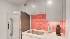 A kitchen with white cabinets, a stainless steel refrigerator, a sink, and a red patterned backsplash. - Let Your Delray Beach Getaway Begin Here! (Delray Beach)