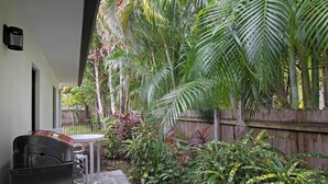 A patio area with a barbecue grill, a table, and a variety of tropical plants. - Let Your Delray Beach Getaway Begin Here! (Delray Beach)