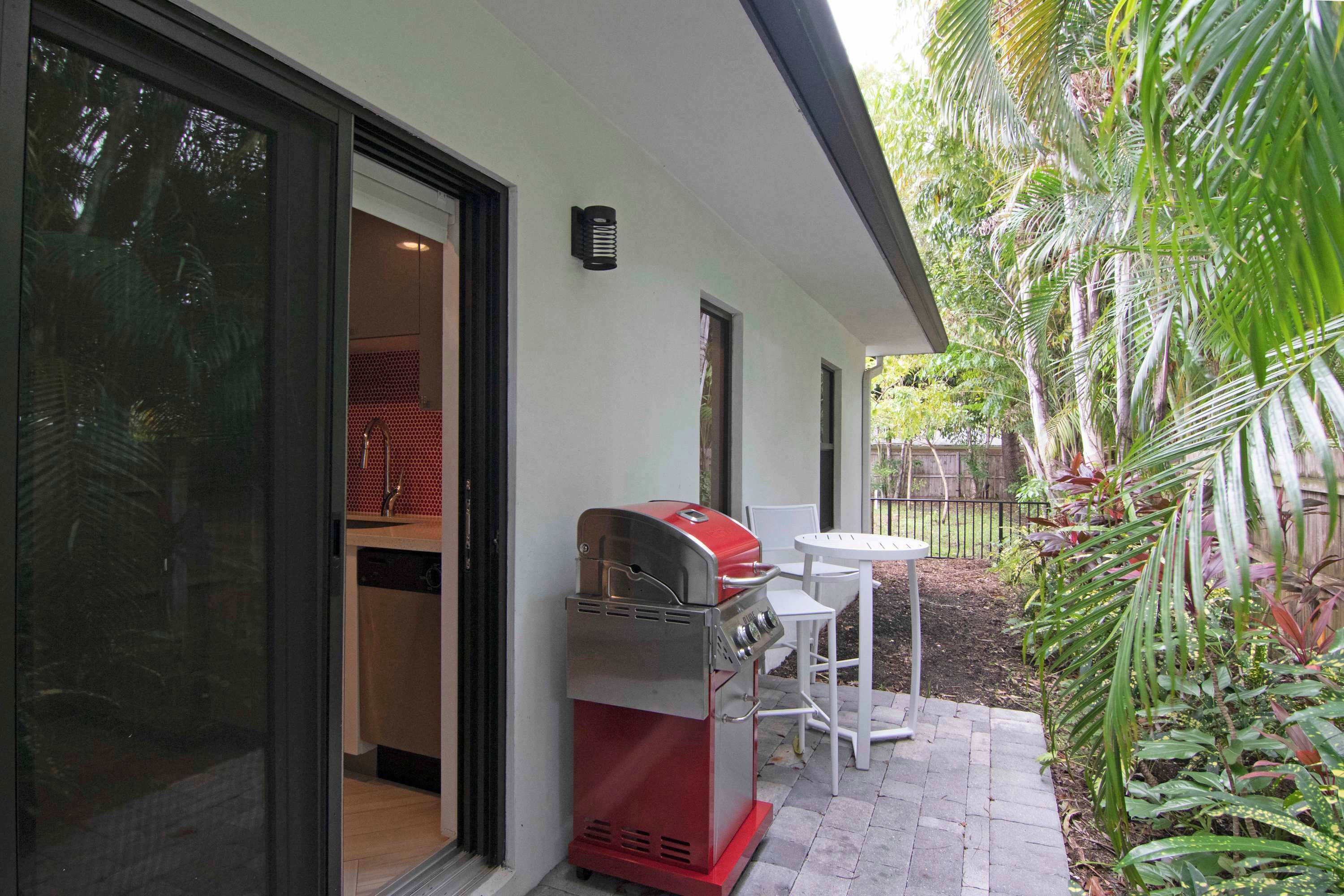 A patio with a red barbecue grill, a white table, and chairs.