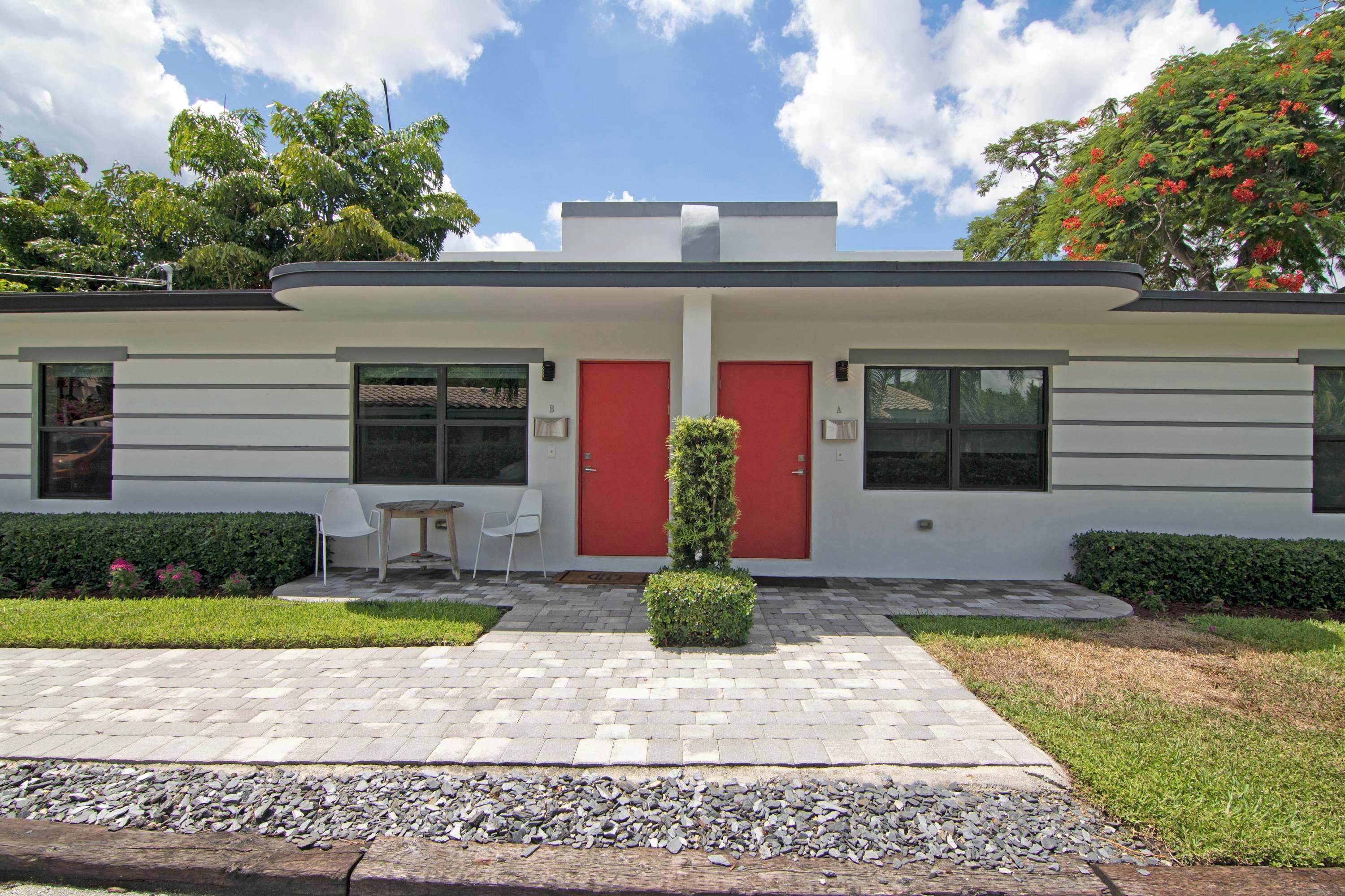 A modern building with a red door, a small patio with a table and chairs, and a well-maintained garden.
