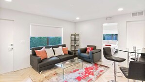 A modern living room with a glass coffee table, two sofas, a dining area with a glass table, and a view of a garden through large windows. - Let Your Delray Beach Getaway Begin Here! (Delray Beach)