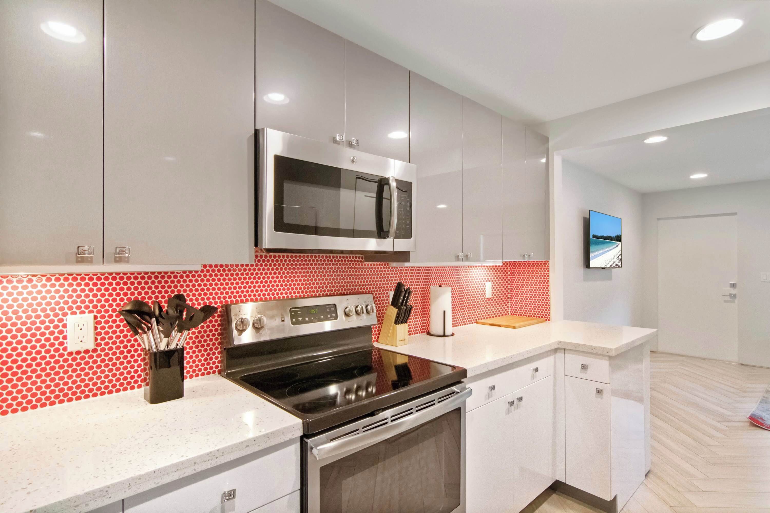 A modern kitchen with stainless steel appliances, a microwave, and a red patterned backsplash.