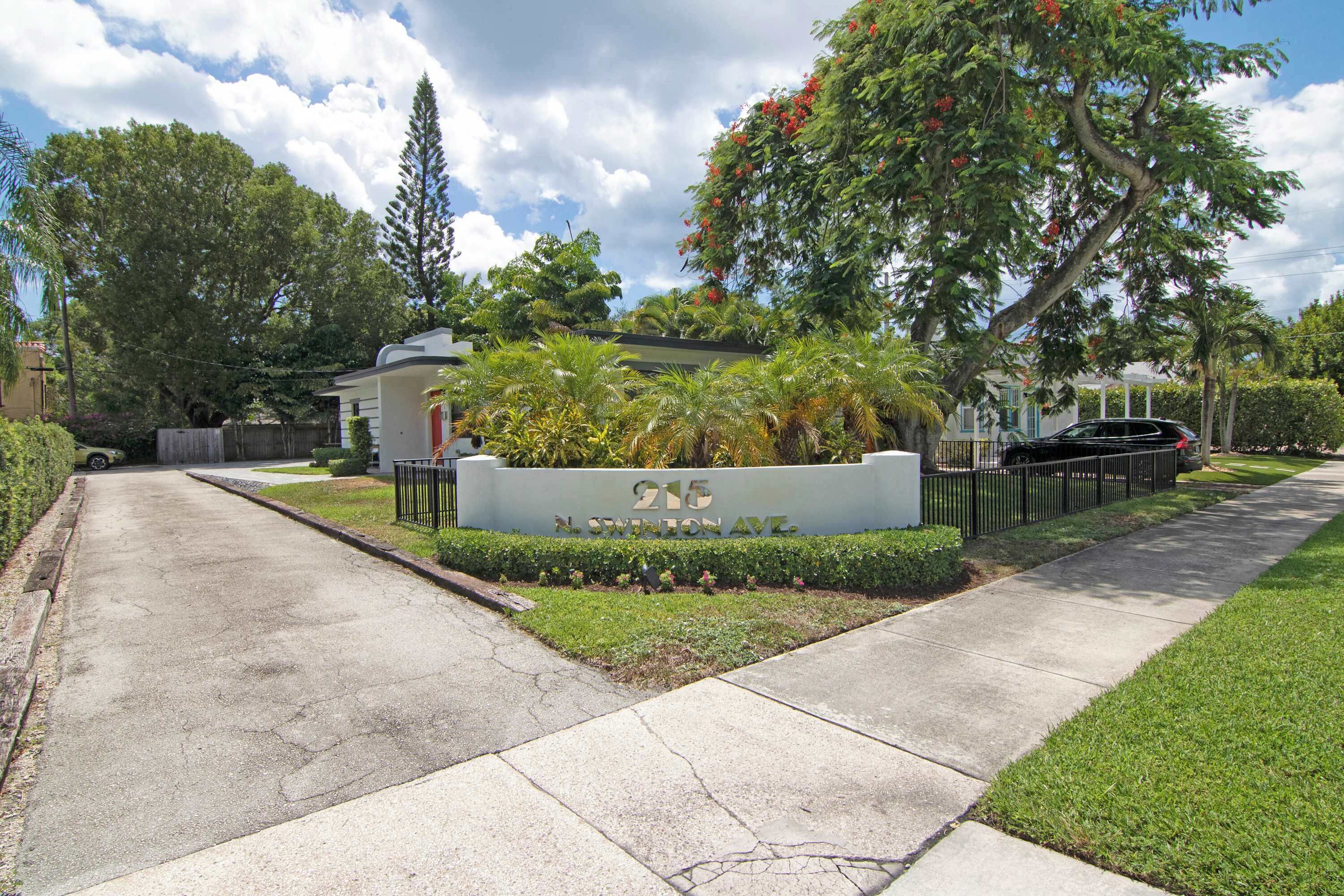 A residential street with a house number sign, a sidewalk, and lush greenery.
