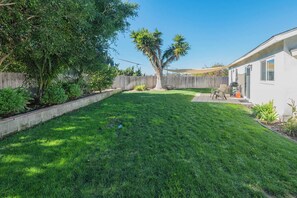 A backyard with a wooden fence, a lawn, and a patio area with outdoor furniture. - Family Retreat, Legoland and the Beach! (Oceanside)