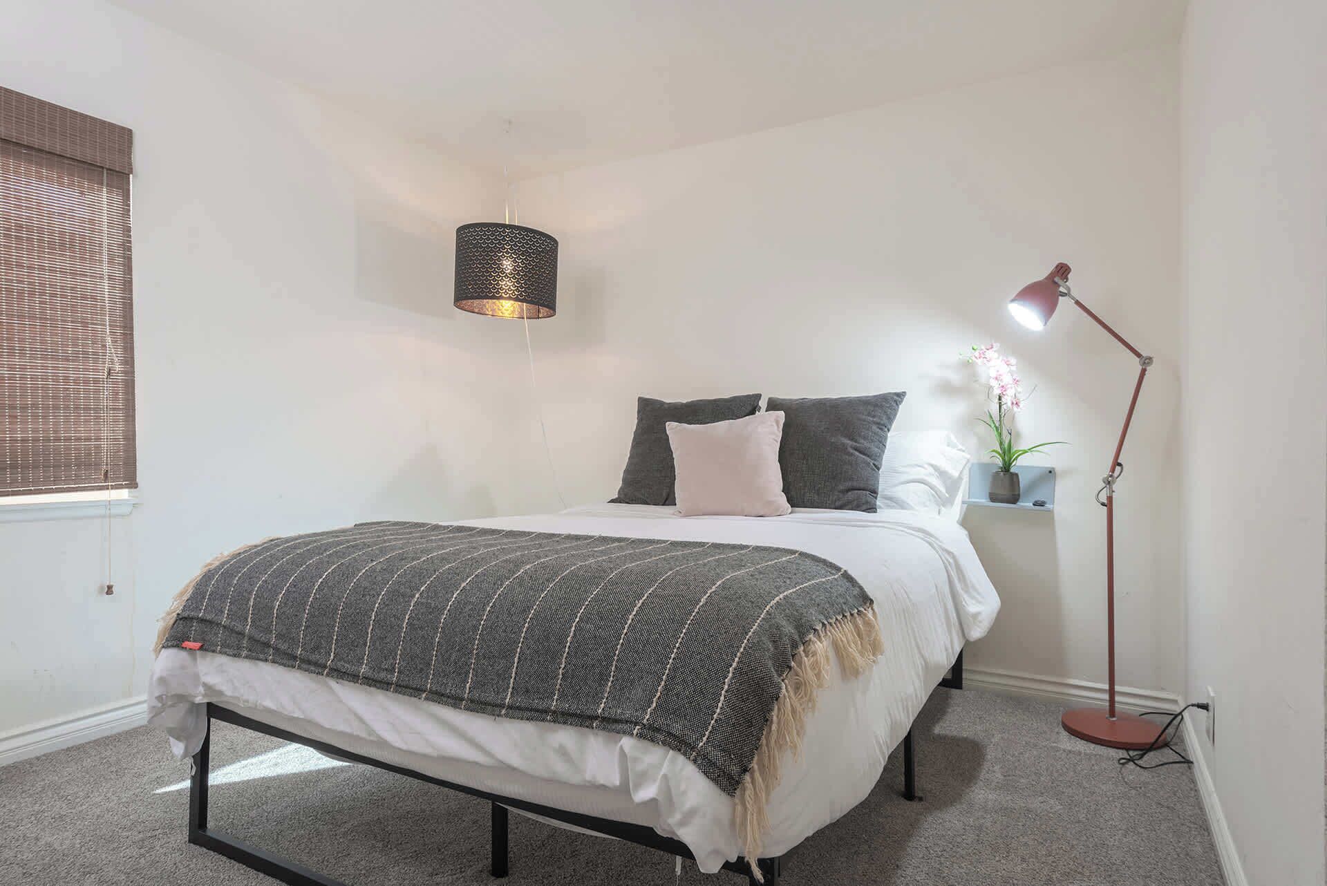 A bedroom with a bed, a bedside lamp, a potted plant, and a hanging light fixture.