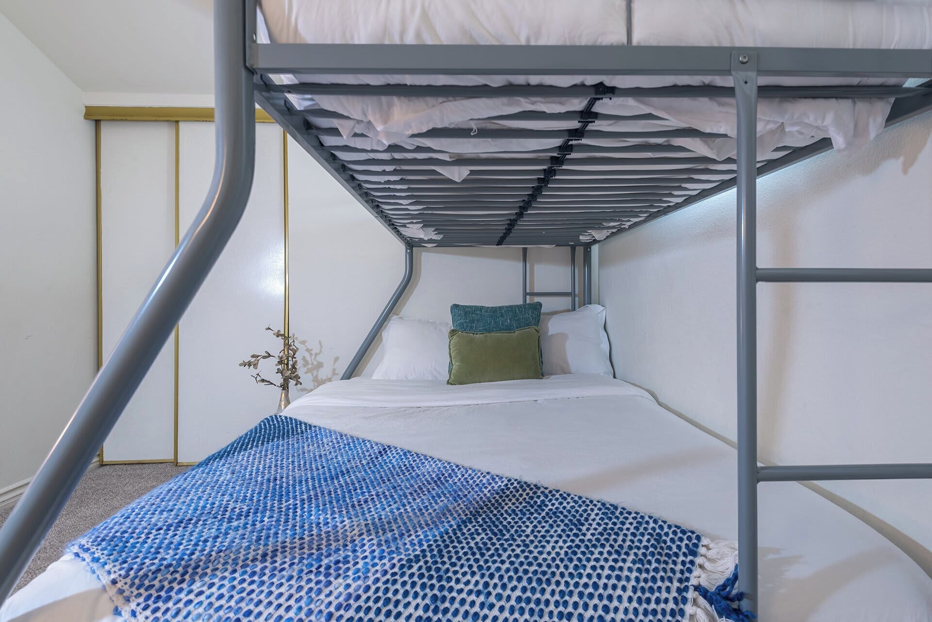 A bunk bed with a metal frame, white bedding, and a blue patterned throw blanket.