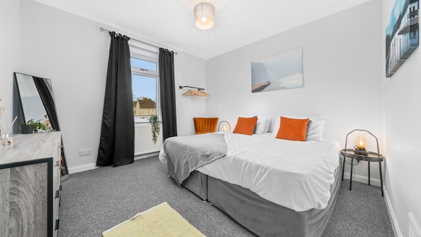 A modern bedroom with a large bed, a desk, and a window with curtains.