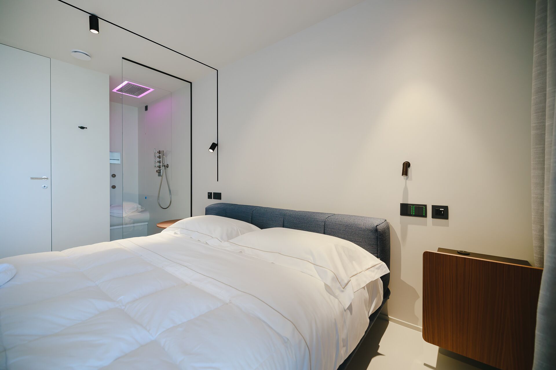 Una camera da letto moderna con un letto, un armadio, un angolo doccia e un comodino.