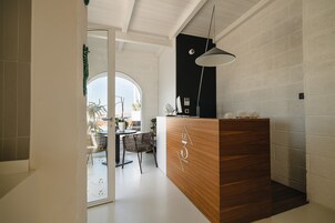 Et moderne receptionområde med et træbord, en hængende pendellampe og udsigt til spiseområdet gennem en glasdør.
