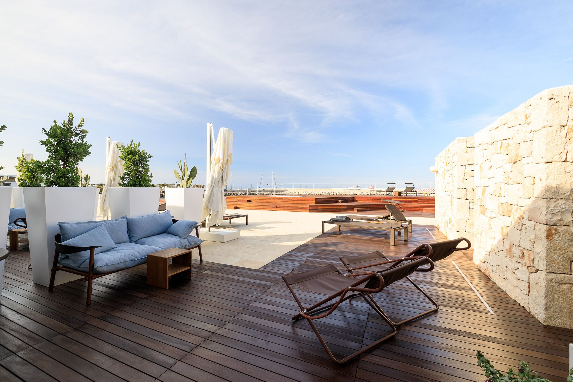 Una terraza en la azotea con suelo de madera, sillones de descanso y un muro de piedra.