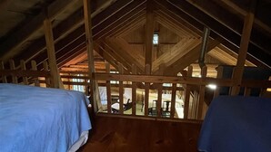 A dormitory room with wooden beams, a sloped ceiling, and two beds with blue bedding.