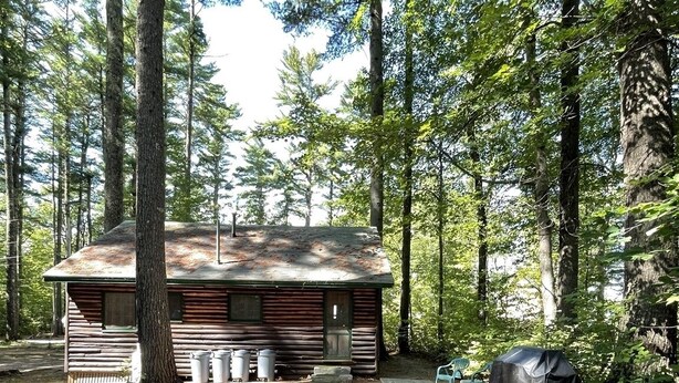 A rustic cabin with a picnic table and chairs, surrounded by tall trees.