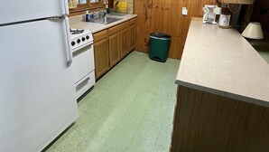 A compact kitchen with wooden walls, a white refrigerator, a stove, and a sink.