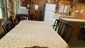 A wooden cabin interior with a dining table, chairs, a refrigerator, a microwave, and a kitchen area.
