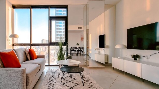 A modern living room with a sofa, a coffee table, a TV, and a dining area with chairs and a table.