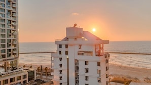 A high-rise hotel overlooking a beach with a sunset view.