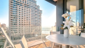 A balcony with a white table and chairs, a vase with white flowers, and a city view.