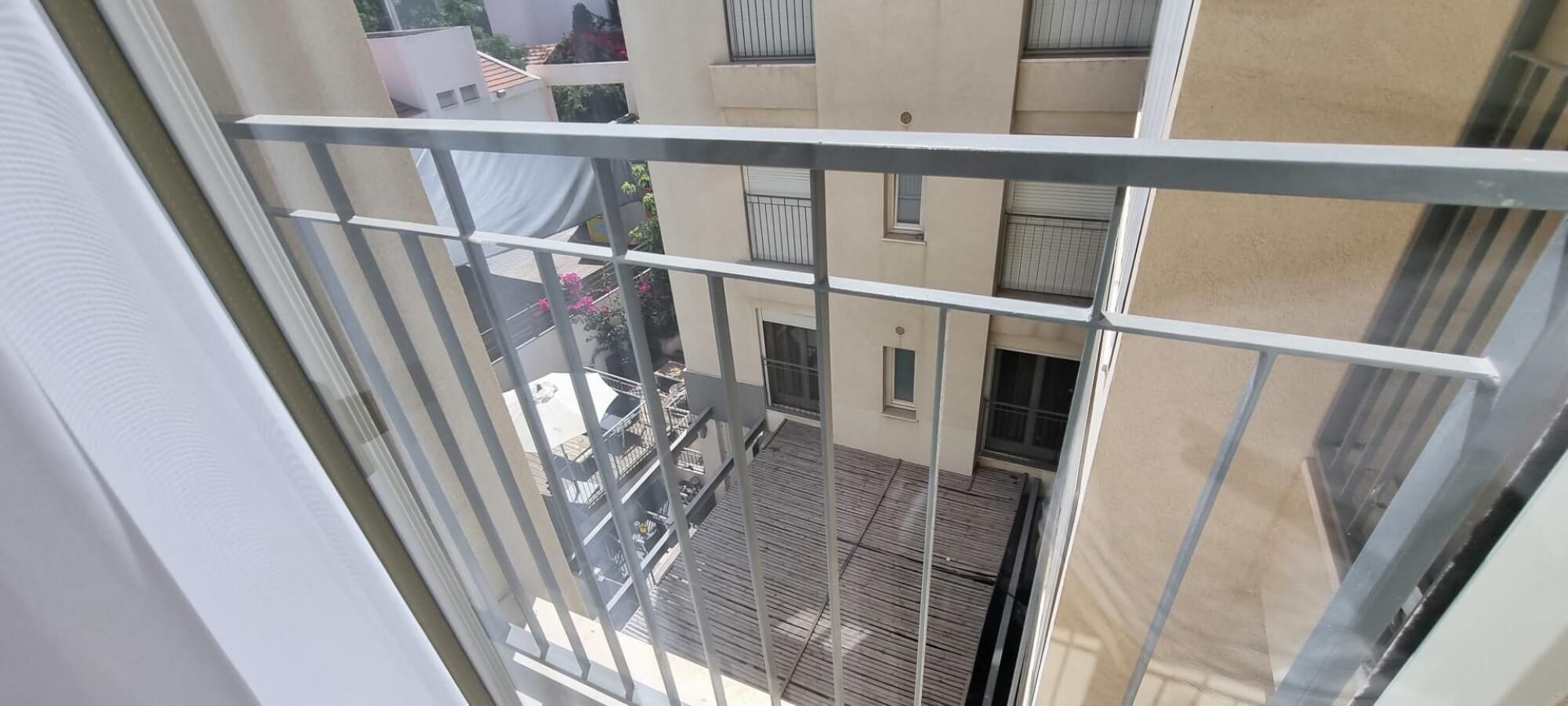 A view from a balcony with a metal railing, overlooking a courtyard with a wooden deck and a building with multiple windows and balconies.