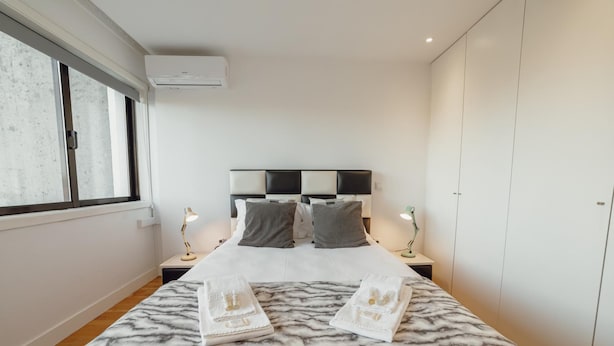 A neatly arranged bedroom with a bed, two bedside lamps, a headboard, and a wardrobe. - Downtown Stylish Apartment Garage by Vacationy (Porto)