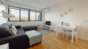 A modern living room with a large window, a sofa, a TV, and a dining area with chairs and a table. - Downtown Stylish Apartment Garage by Vacationy (Porto)