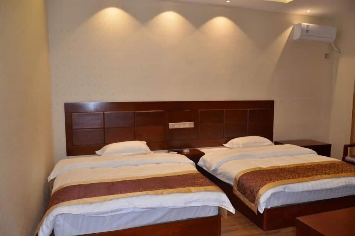 A hotel room with two beds, a wooden headboard, a nightstand, and an air conditioning unit.