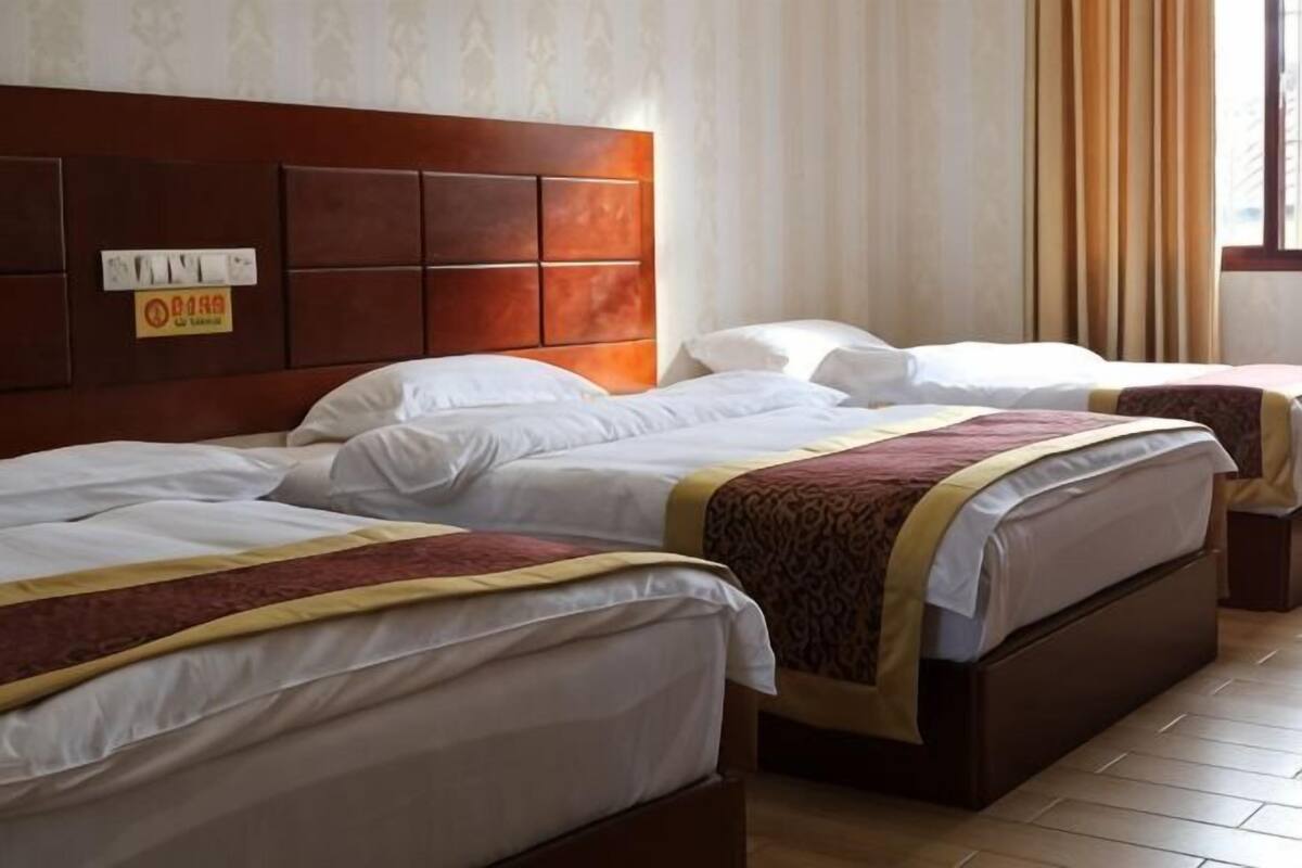 A hotel room with three beds, a wooden headboard, and a window with curtains.