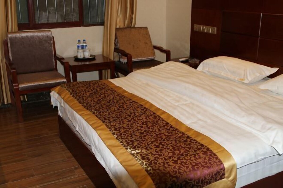 A hotel room with a bed, a chair, a small table with water bottles, and a wooden wardrobe.