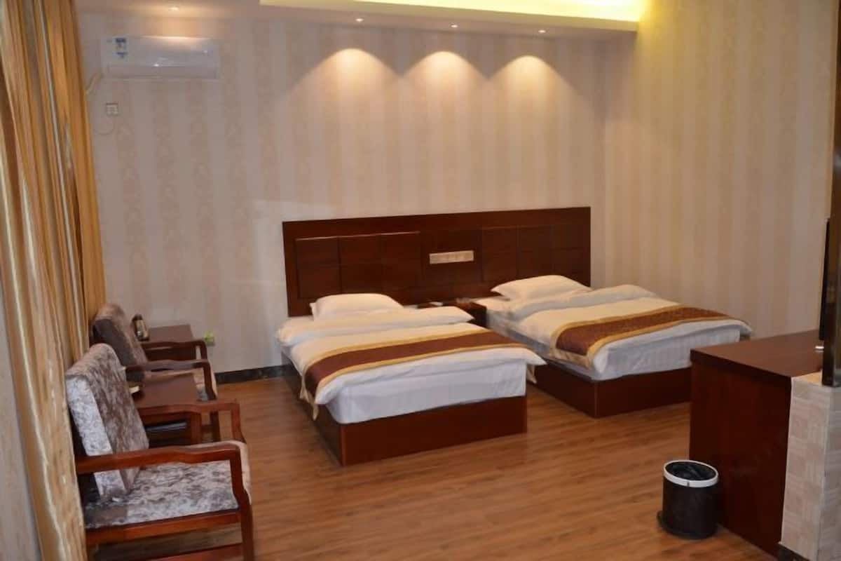 A hotel room with three beds, wooden flooring, a small table, and a chair.