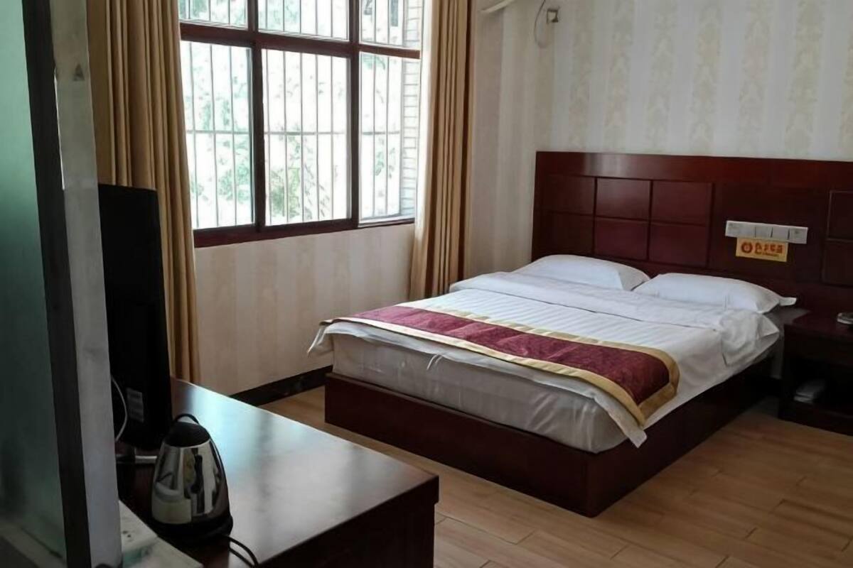 A hotel room with a bed, a bedside table, a TV, and a window with curtains.