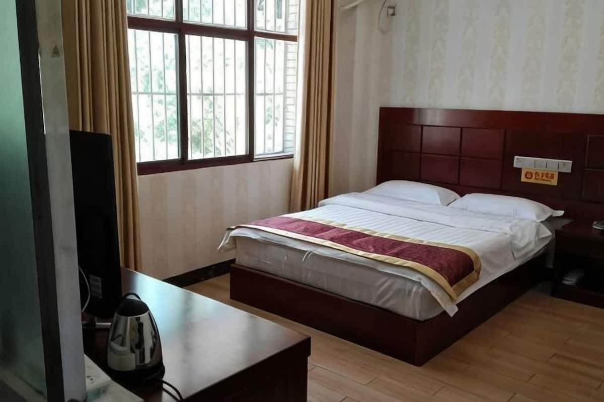 Une chambre d’hôtel avec un lit, une table de chevet, une télévision et une fenêtre avec des rideaux.