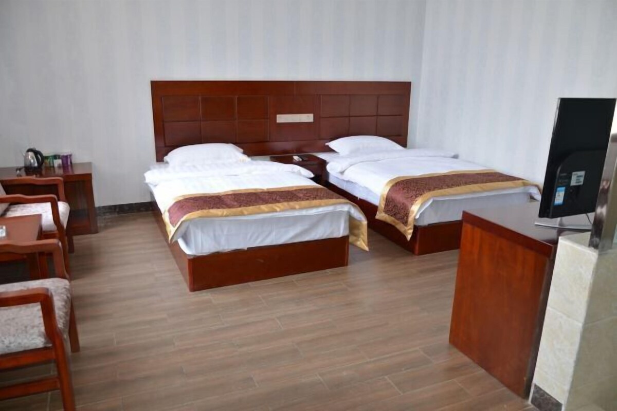 A hotel room with two beds, a desk, a chair, and a television.