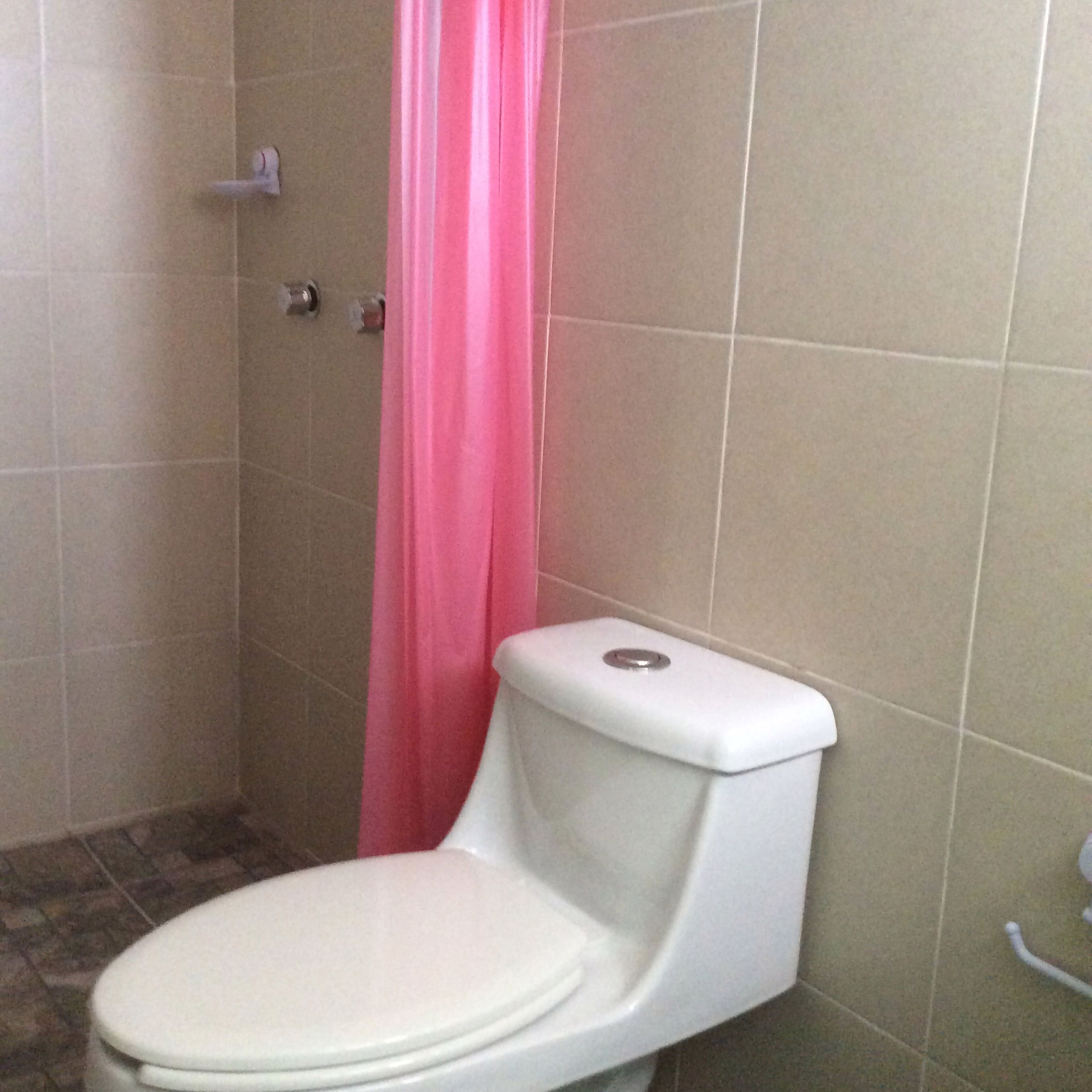 A bathroom with a toilet, a pink shower curtain, and tiled walls.