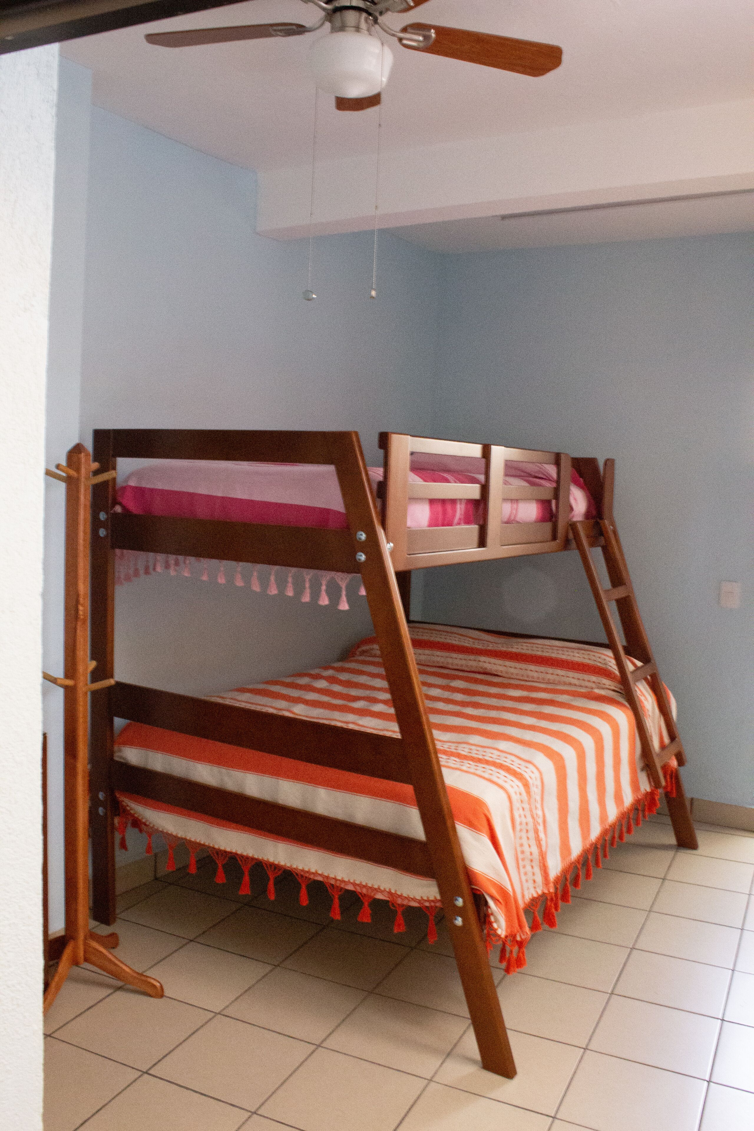 A bunk bed with a wooden frame and orange and white striped bedding.