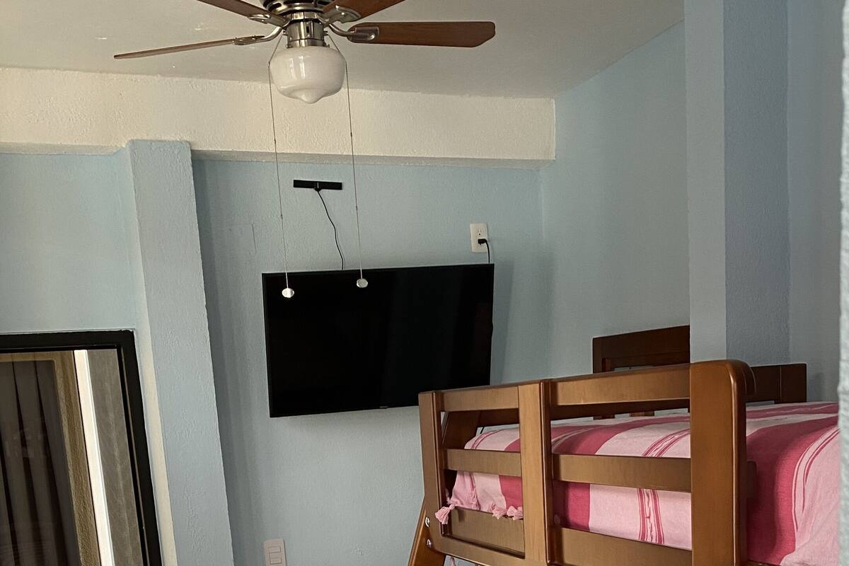 A bedroom with a bunk bed, a ceiling fan, a flat-screen TV, and a chair.