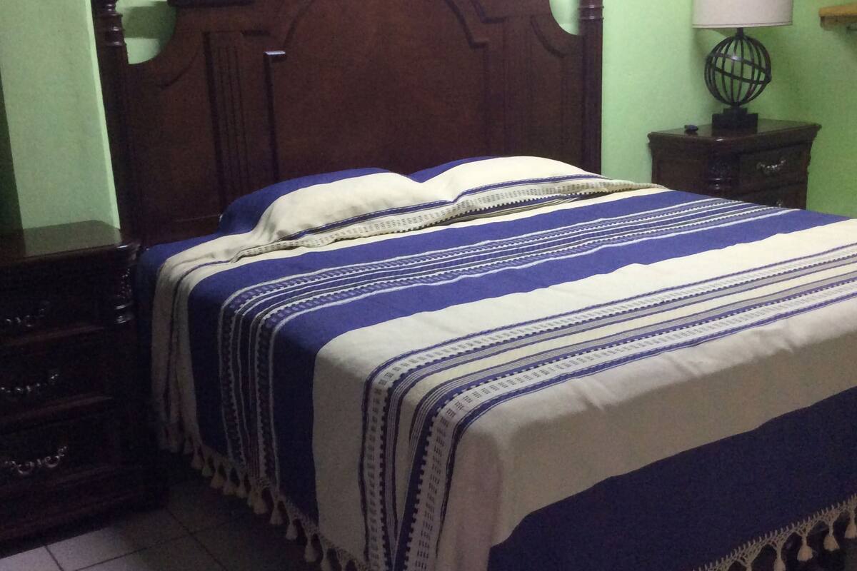 A bedroom with a wooden headboard, a bed with a blue and white striped bedspread, a nightstand with a lamp, and a green wall.