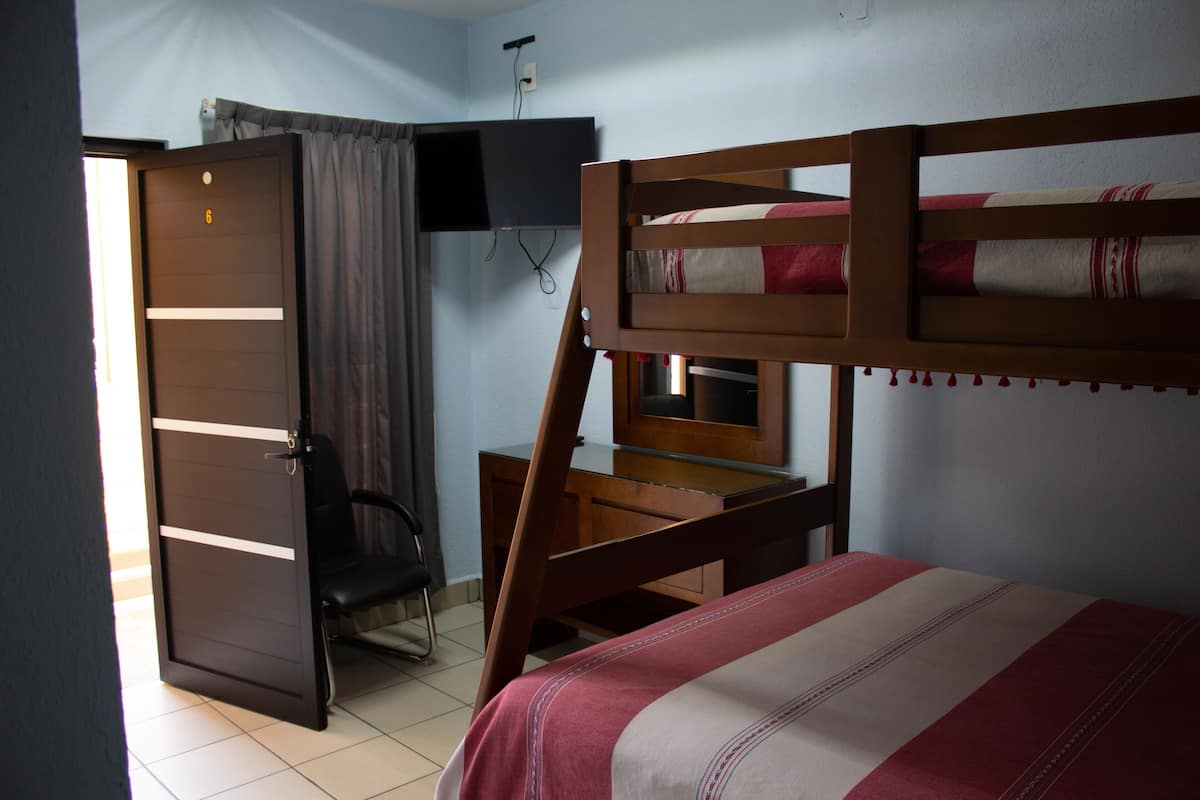 A room with a bunk bed, a desk with a chair, a television mounted on the wall, and a door.
