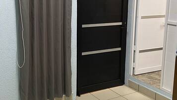 Une pièce avec une porte noire fermée, un rideau gris et un sol carrelé.
