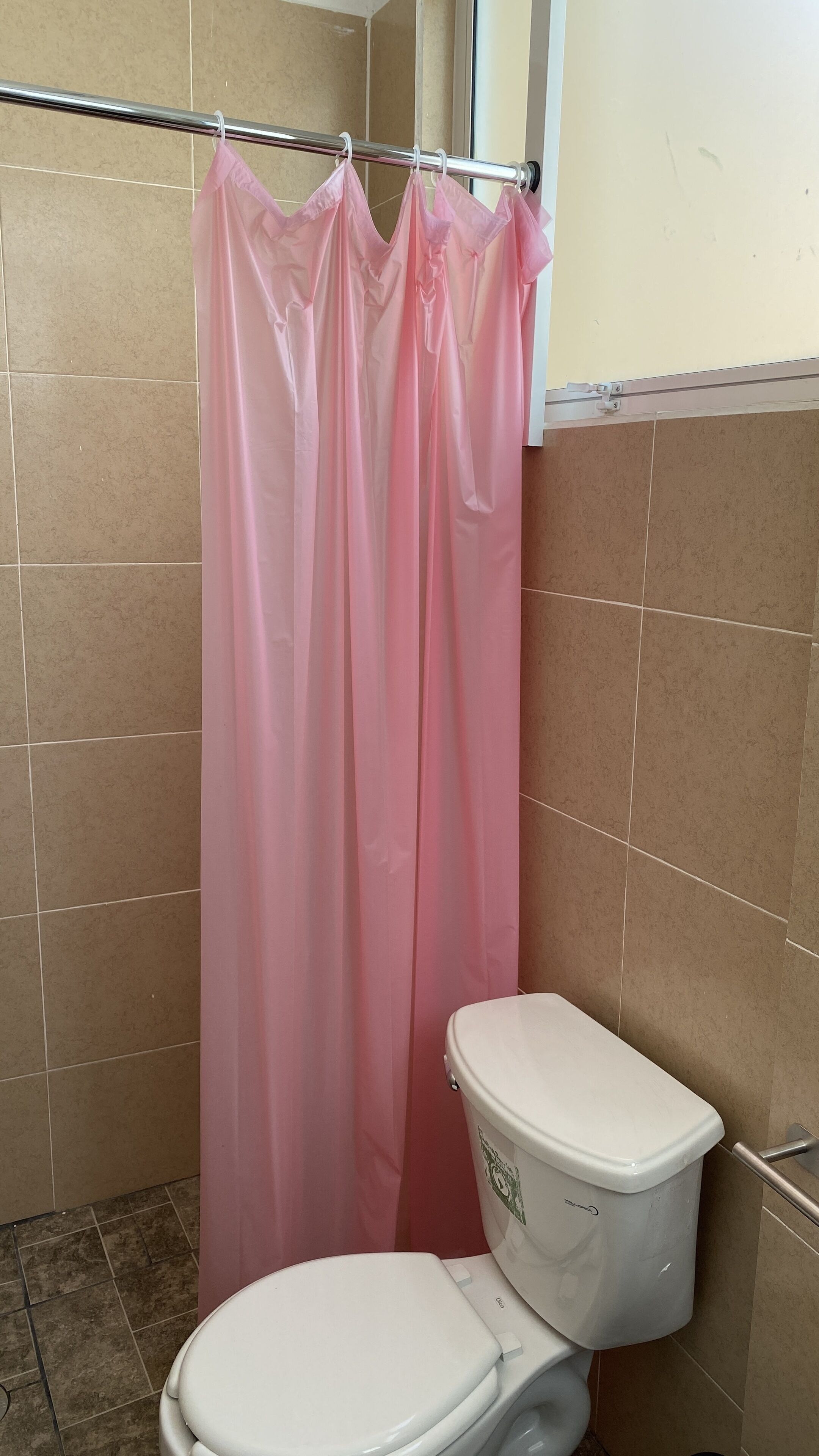 A bathroom with a white toilet, a pink shower curtain, and beige tiled walls.