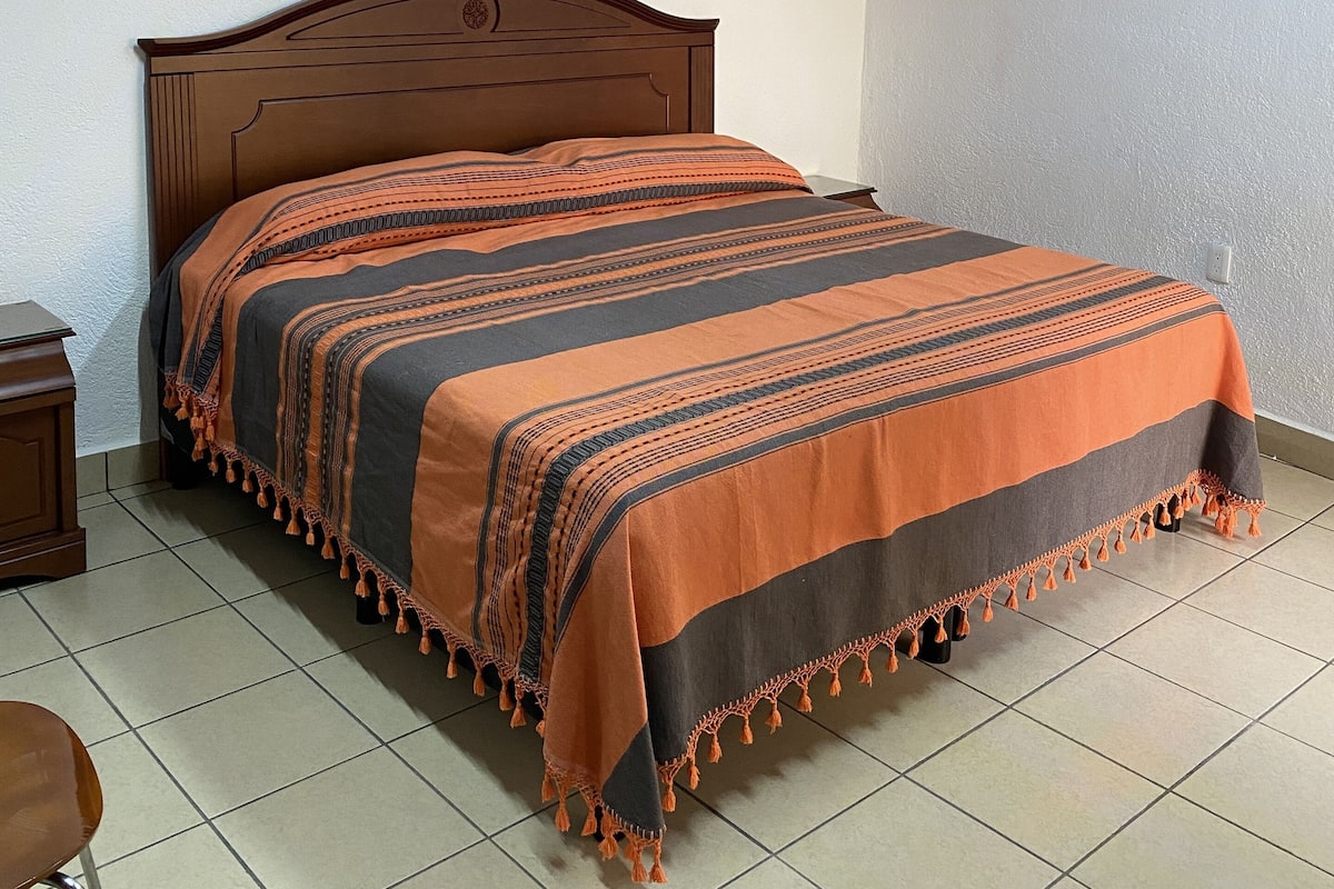 A bed with a patterned blanket, a wooden headboard, a nightstand, and a chair.