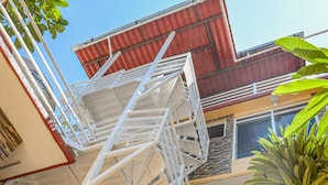 Un edificio de varios pisos con una escalera espiral blanca, una palmera y un techo rojo.