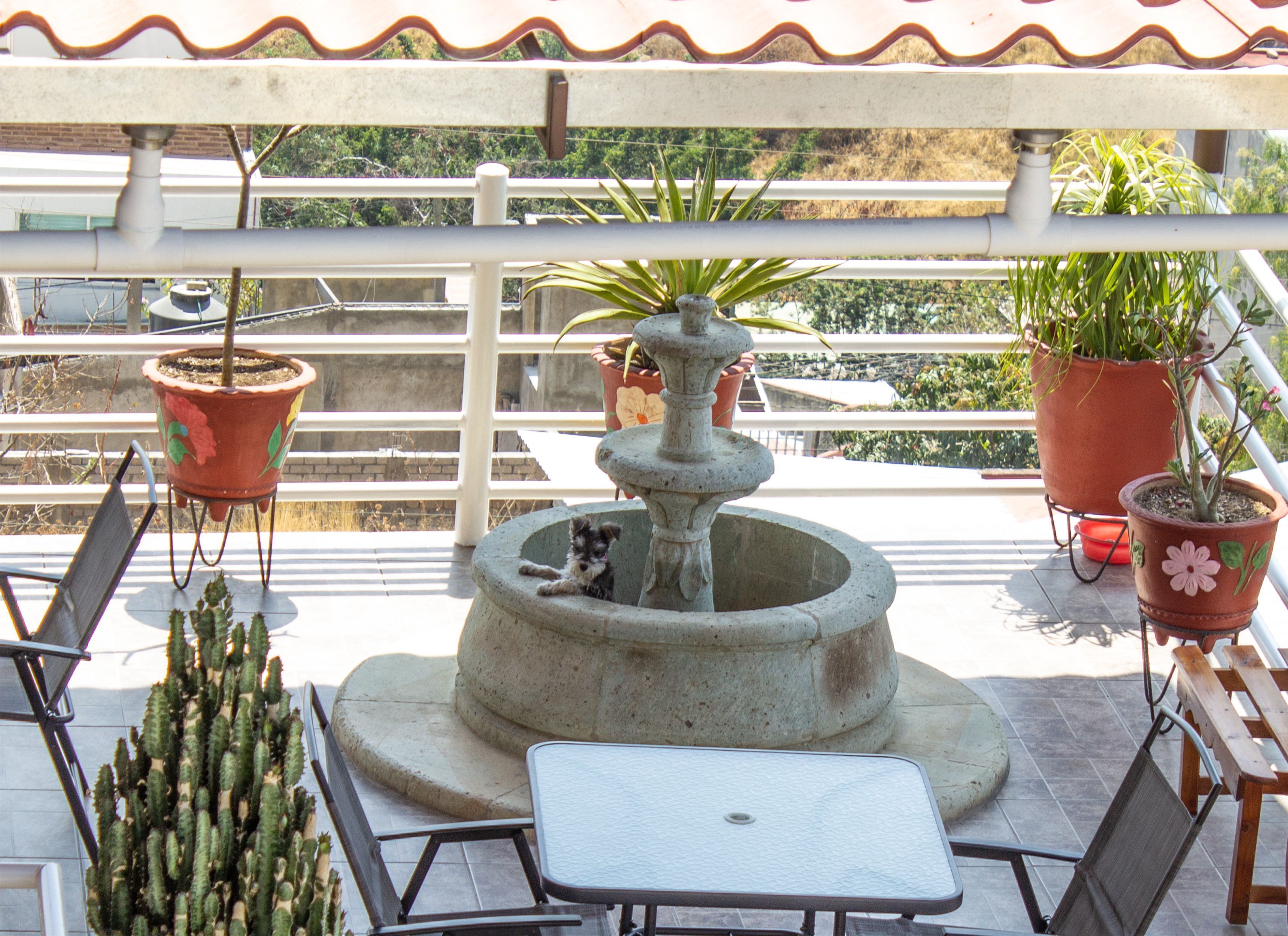 A balcony with a stone fountain, potted plants, and outdoor furniture.