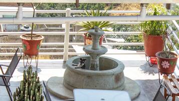 A balcony with a stone fountain, potted plants, and outdoor furniture.