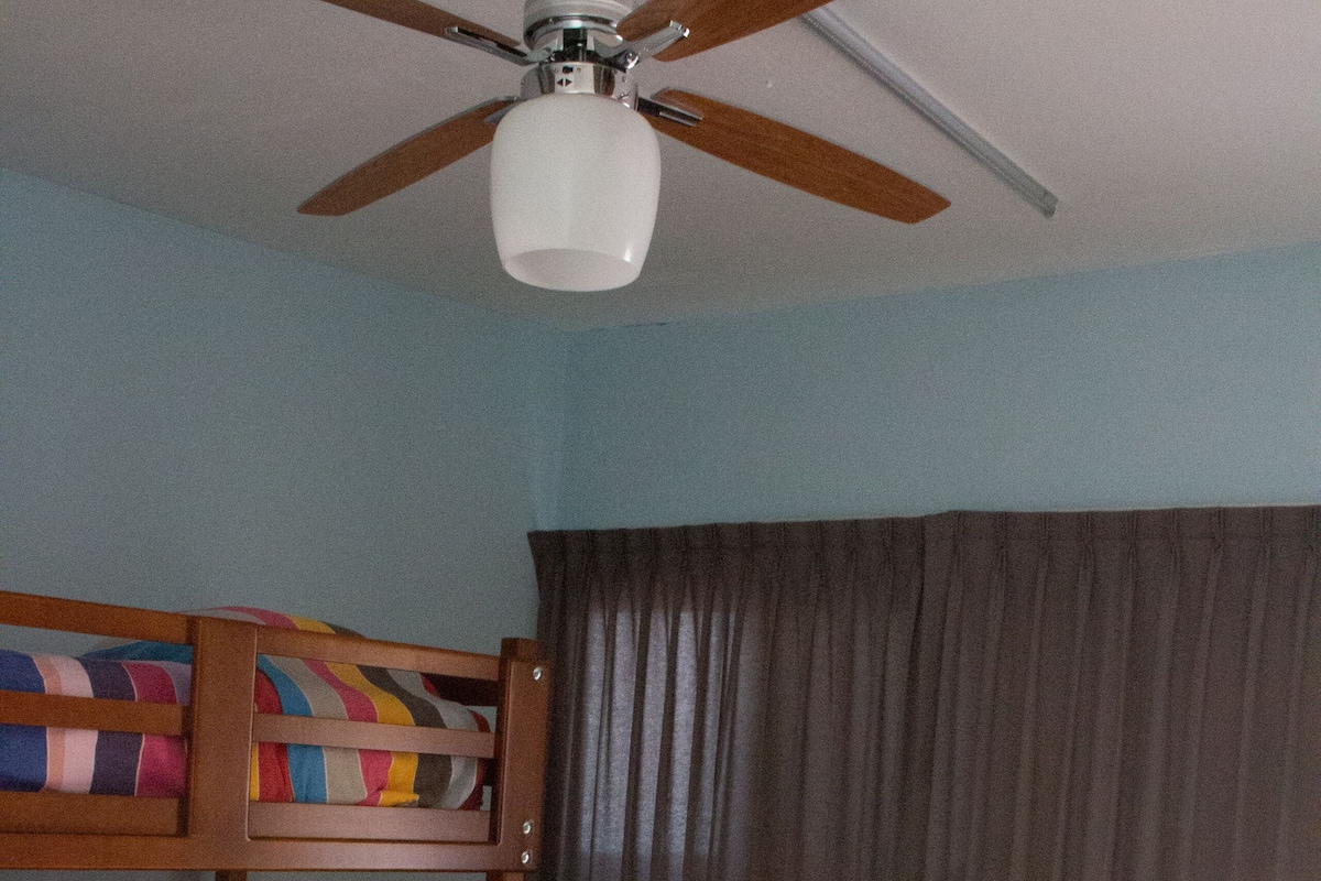 A room with a bunk bed, a ceiling fan, and a window with curtains.