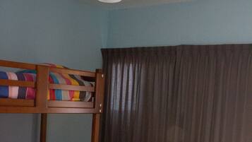 A room with a bunk bed, a ceiling fan, and a window with curtains.