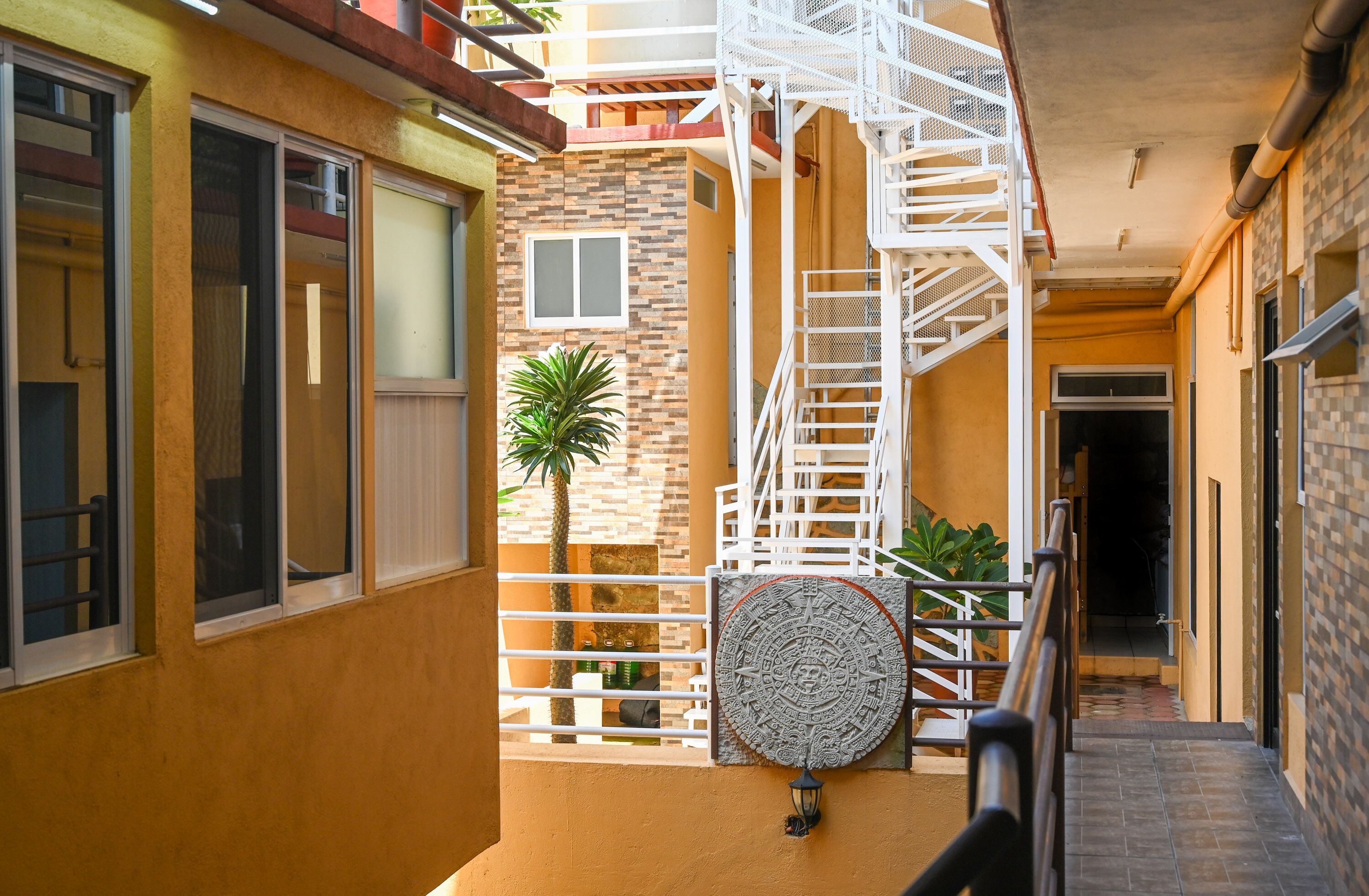 Ein schmaler Korridor mit einem weißen Metallgeländer, einer Wendeltreppe und einer Tür zu einem Innenraum.