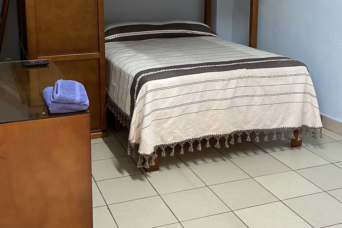A bunk bed with a wooden frame, a ceiling fan, and a bedside table with a towel.