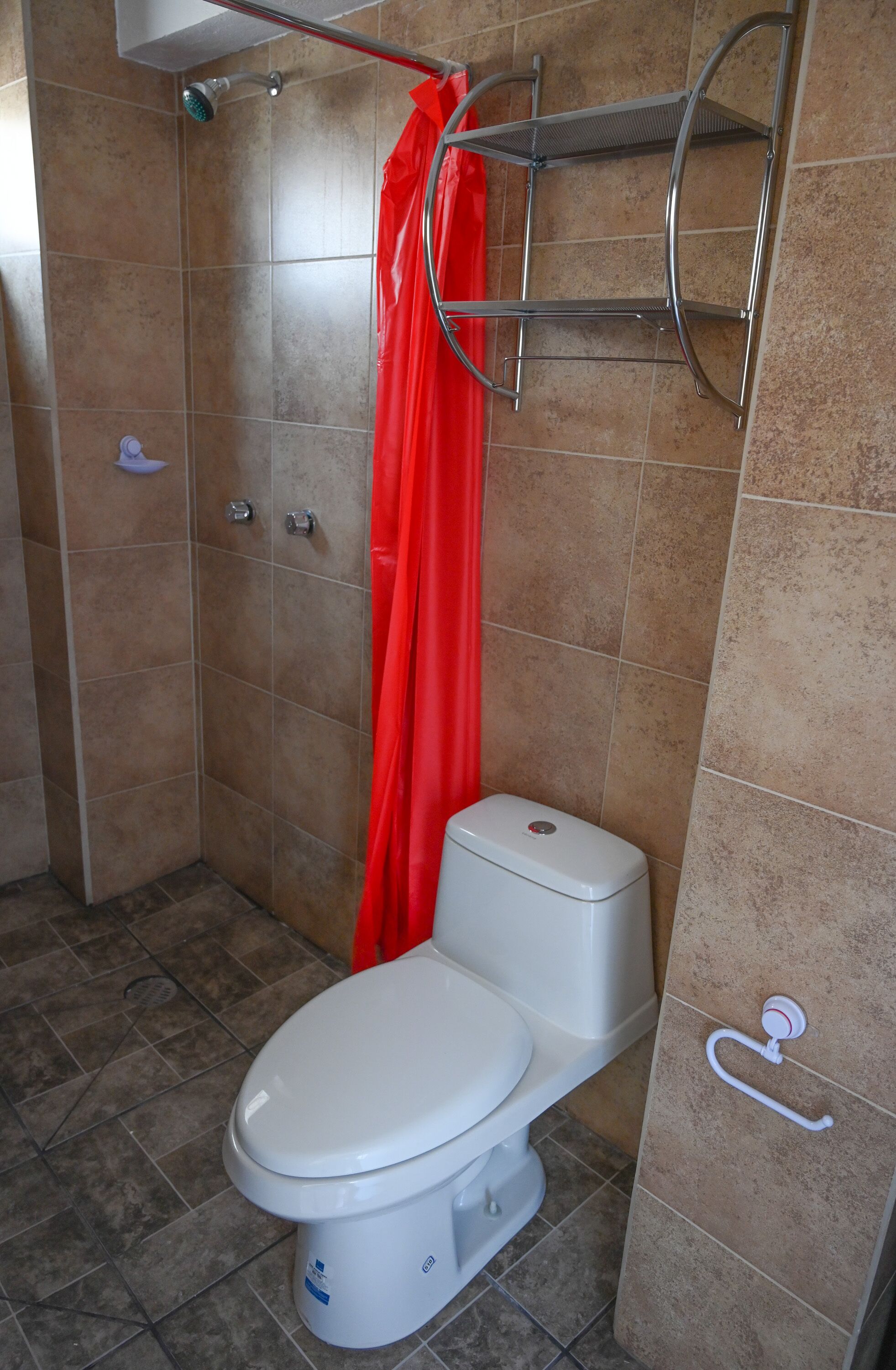 A bathroom with a white toilet, a shower with a red curtain, and a metal shelf.